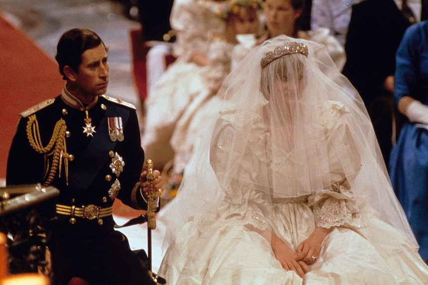 Prince Charles dressed in a uniform and Princess Diana in a wedding dress and veil sit down