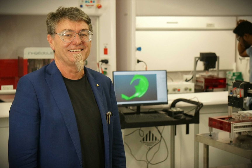 Gordon Wallace stands in a lab in front of a 3D printing machine.