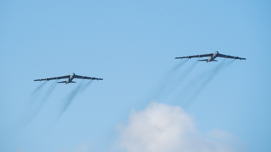 Two US Air Force B-52 H planes fly across a blue sky