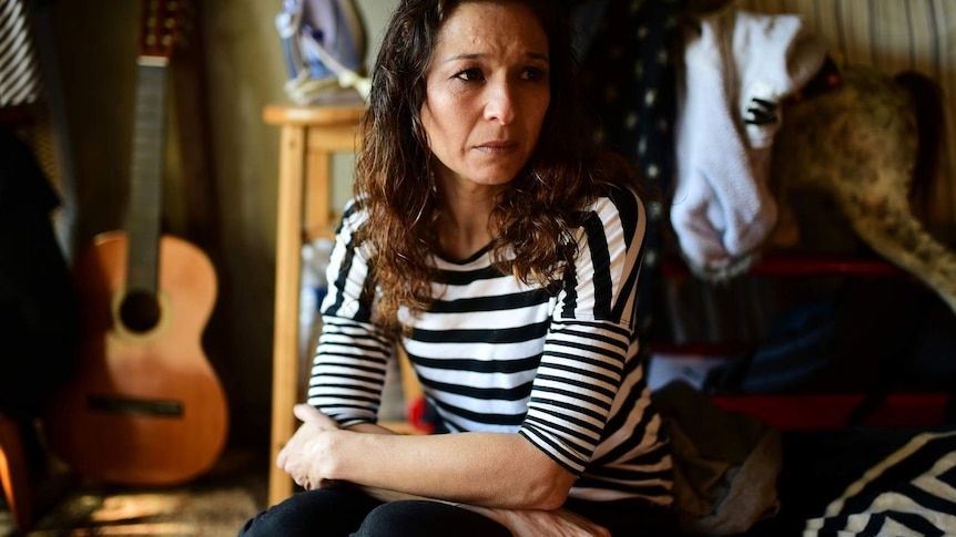 A woman with a sad expression sitting on a mattress in a garage