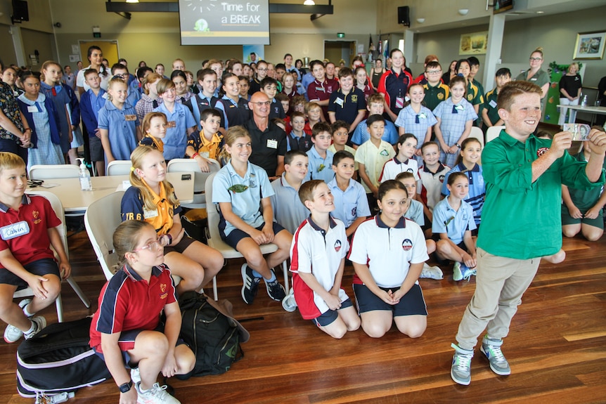 A young boy in front of a crowd of schoolchildren.