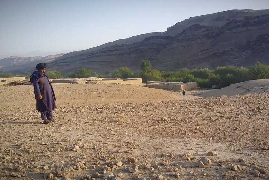 A man standing in the desert with a village on the horizon.