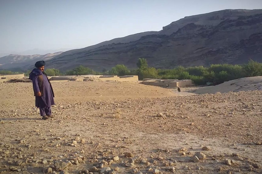 A man standing in the desert with a village on the horizon.