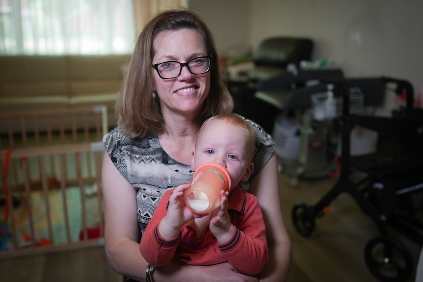 A white woman with brown hair and glasses with a toddler on her lap. The toddler is sipping from a cup