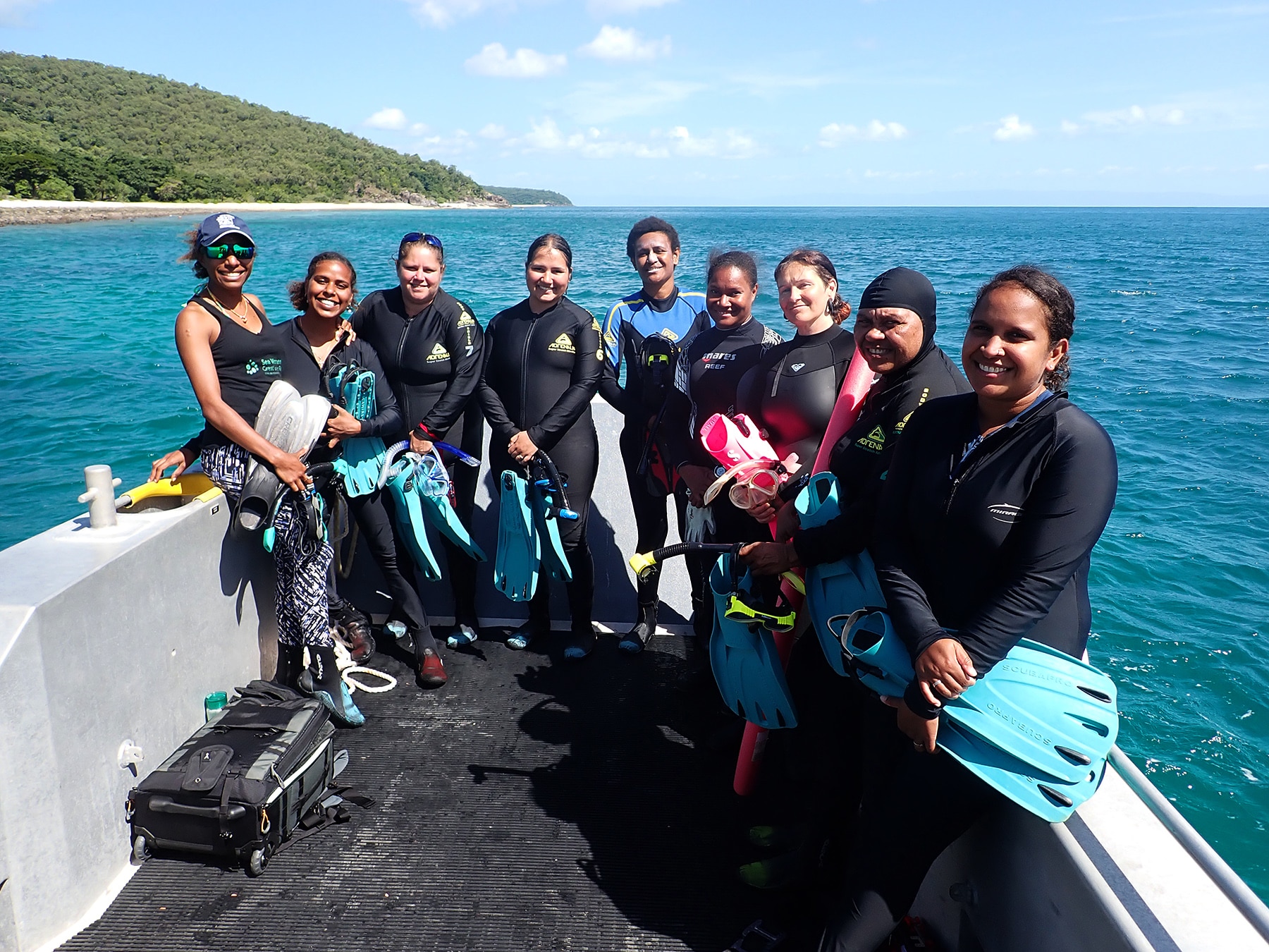 Nine women stand on a boat wearing wetsuits.