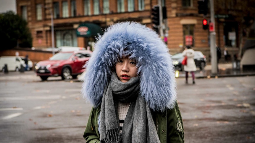 A woman with a big fluffy hood on crosses the street