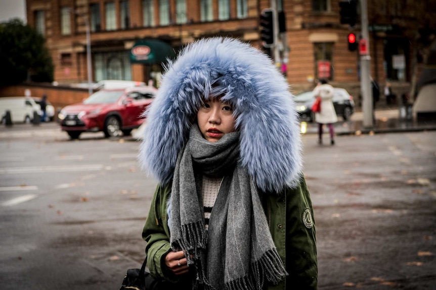 A woman with a big fluffy hood on crosses the street