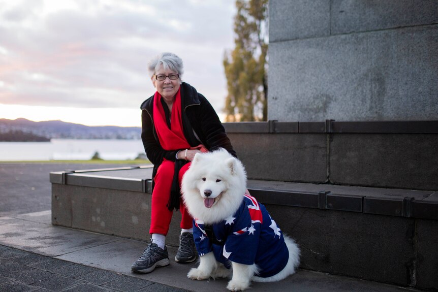 A woman sits on the step of a cenotaph with a dog draped in an Australian flag