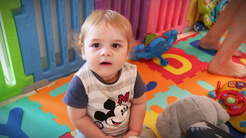 Baby boy sits on colourful floor in playpen
