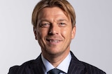 Tony Gustavsson, wearing a nice black suit, folds his arms and smiles for a photo