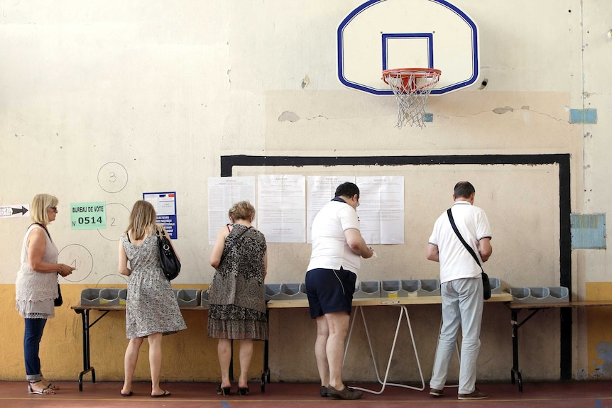 Voters pick up ballots from a table at a polling station before voting.