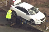 An aerial photo of a white car with emergency services people surrounding it