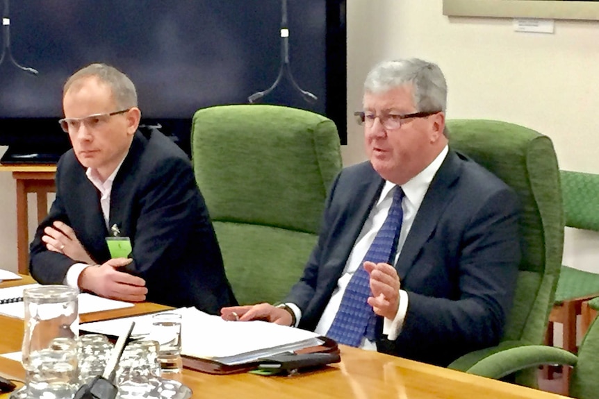 Two men sit at a board room table.