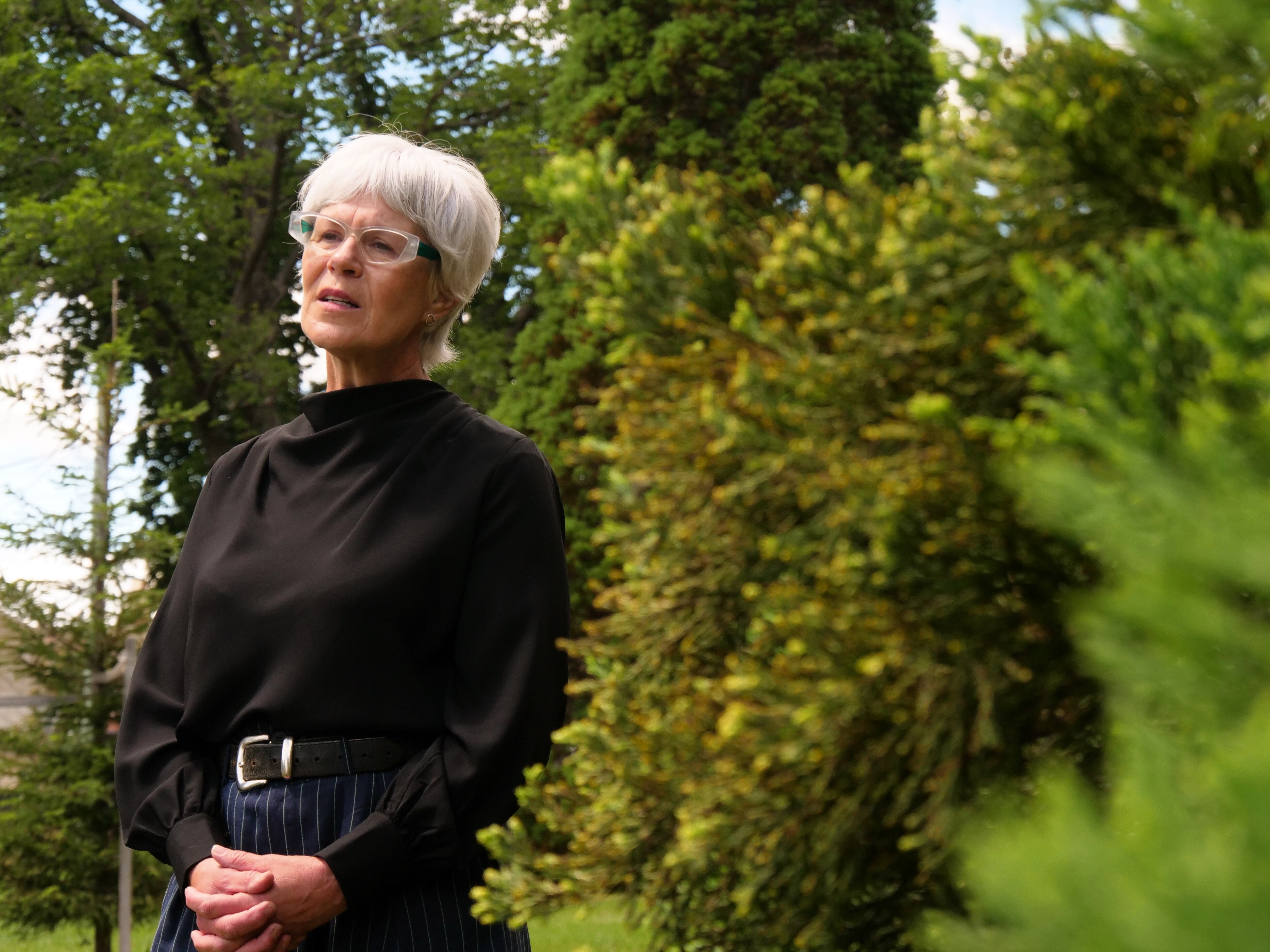 Uma mulher de cabelos brancos e blusa preta está em um parque.