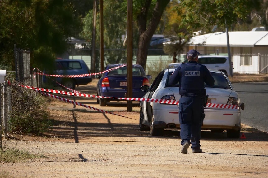 A police officer has his back to the camera as he walks towards some police tape.