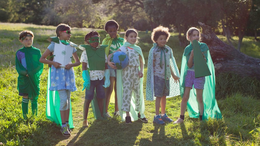 A group of children dressed in green eco warrior costumes, gather under a tree