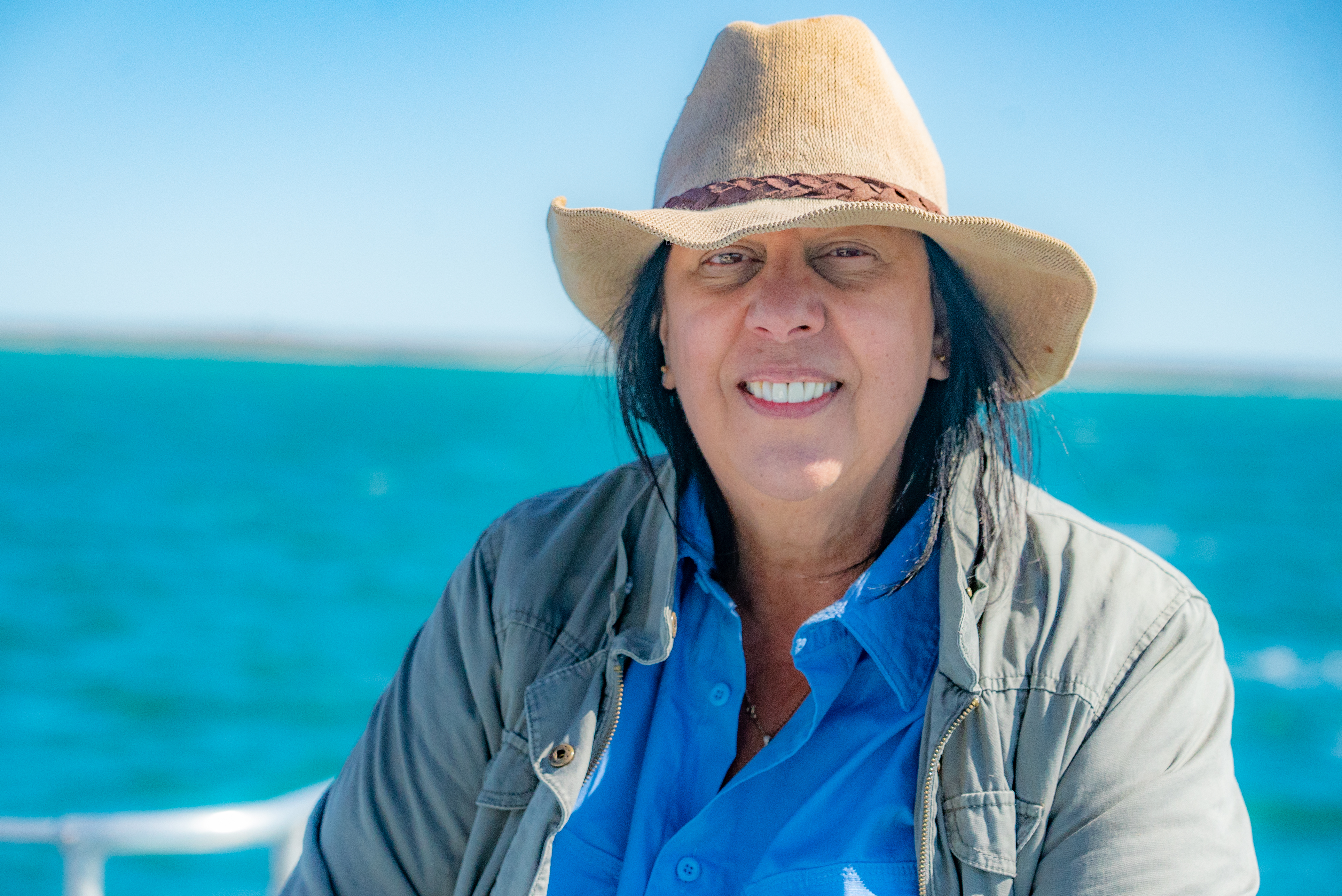 Une femme dans un chapeau de paille sourit avec l'océan en arrière-plan