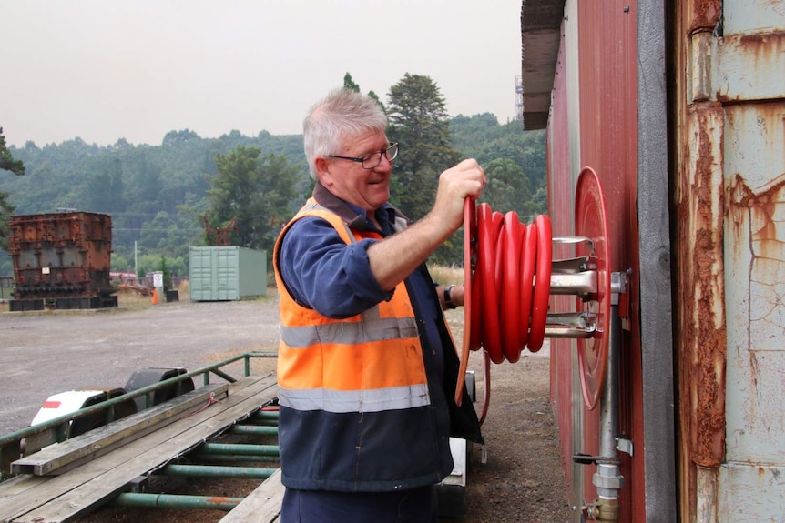 A man wearing a high-vis vest over his jumper turns the wheel of a firehose.