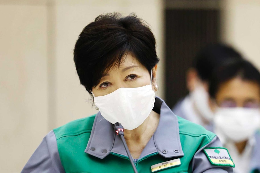 Woman with short dark hair and mask in green uniform