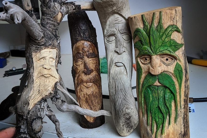 4 different carved faces into logs, the one on the right with green hair and beard