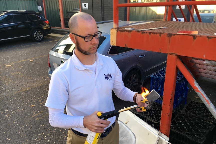 Man putting a torch to a square of metal.