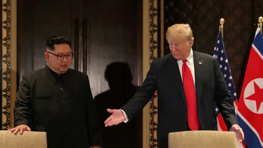 Donald Trump gestures to a chair as he and Kim Jong-un prepare to sign a document.