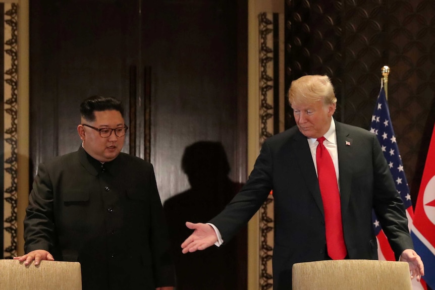 Donald Trump gestures to a chair as he and Kim Jong-un prepare to sign a document.