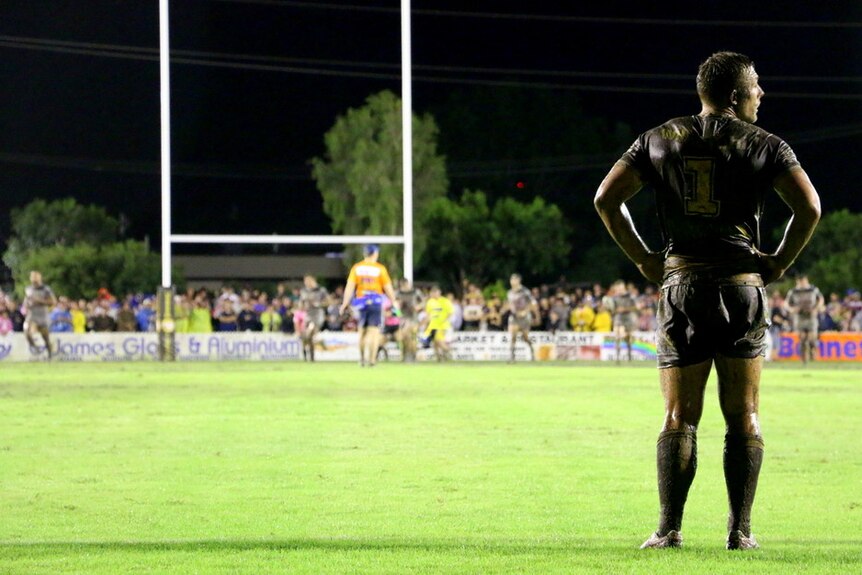 Broncos fullback Greg Eden stands muddy in the foreground, the goal posts off in the distance.