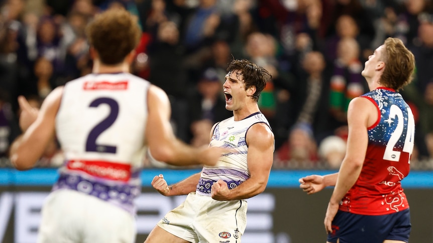 Fremantle's Lachie Schultz pumps his fists and roars with delight as a teammate runs toward him and an opponent looks dejected.