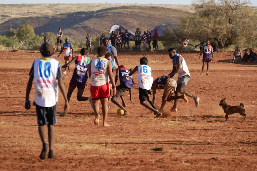 Men playing football on a red dirt field.