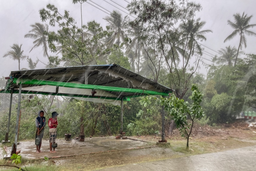 Two children stand under a roadside shelter to protect from rain before Cyclone Mocha hits.