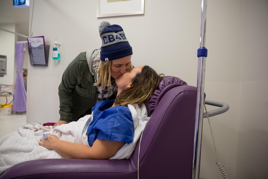 Bec kisses her partner Sharon who lies in a hospital bed.