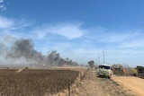 A fire truck on a dirt road next to a crop with smoke behind