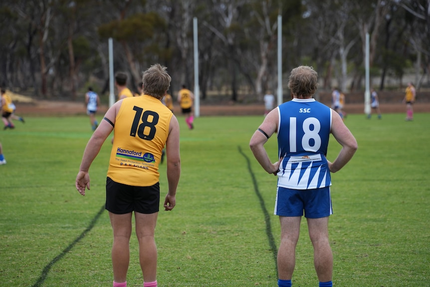 Two players on opposing teams both wearing the number 18 jersey look down the football over. 