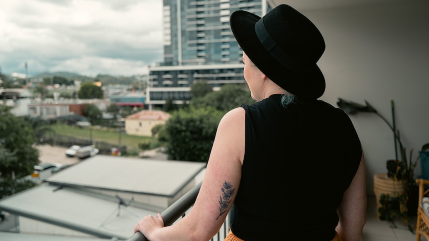 a woman with her back to the camera, looking over a high rise balcony onto inner brisbane