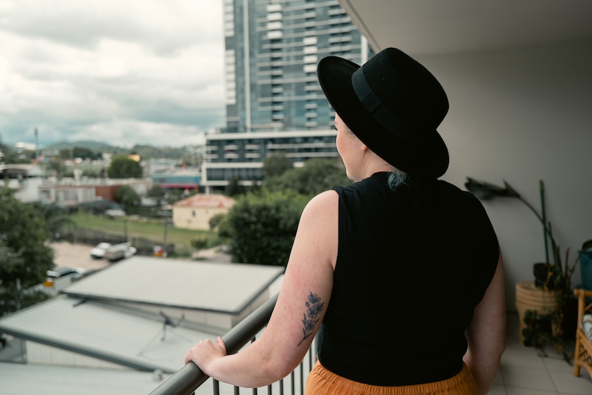 a woman with her back to the camera, looking over a high rise balcony onto inner brisbane