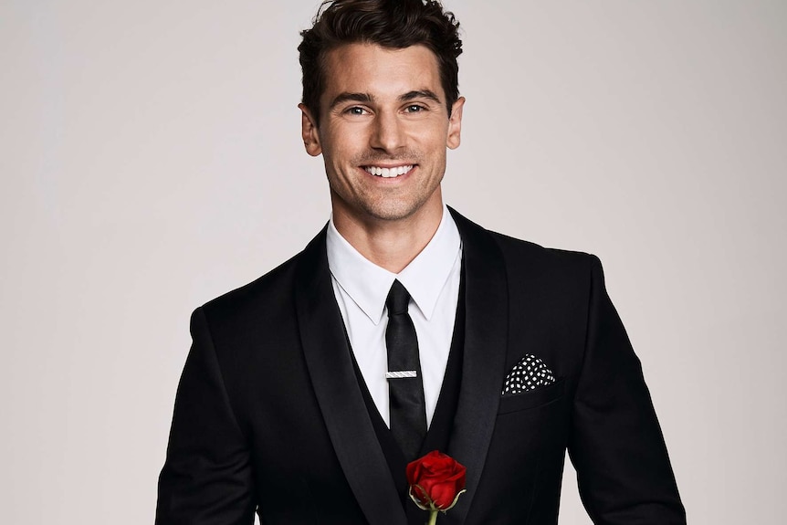 A smiling man holds a red rose