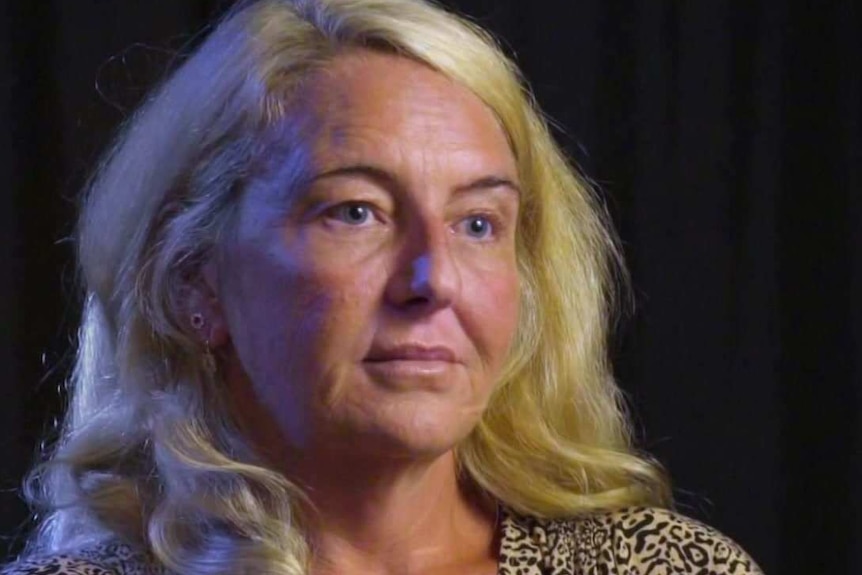 A portrait of a woman with long blonde hair wearing a dress in a black room.