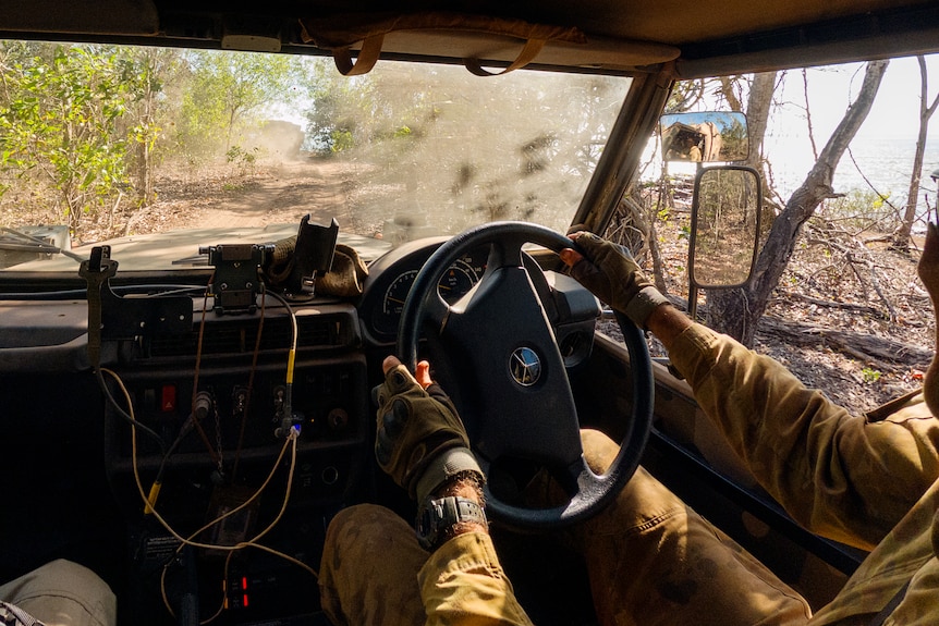 a person wearing army uniform driving a vehicle through bushland
