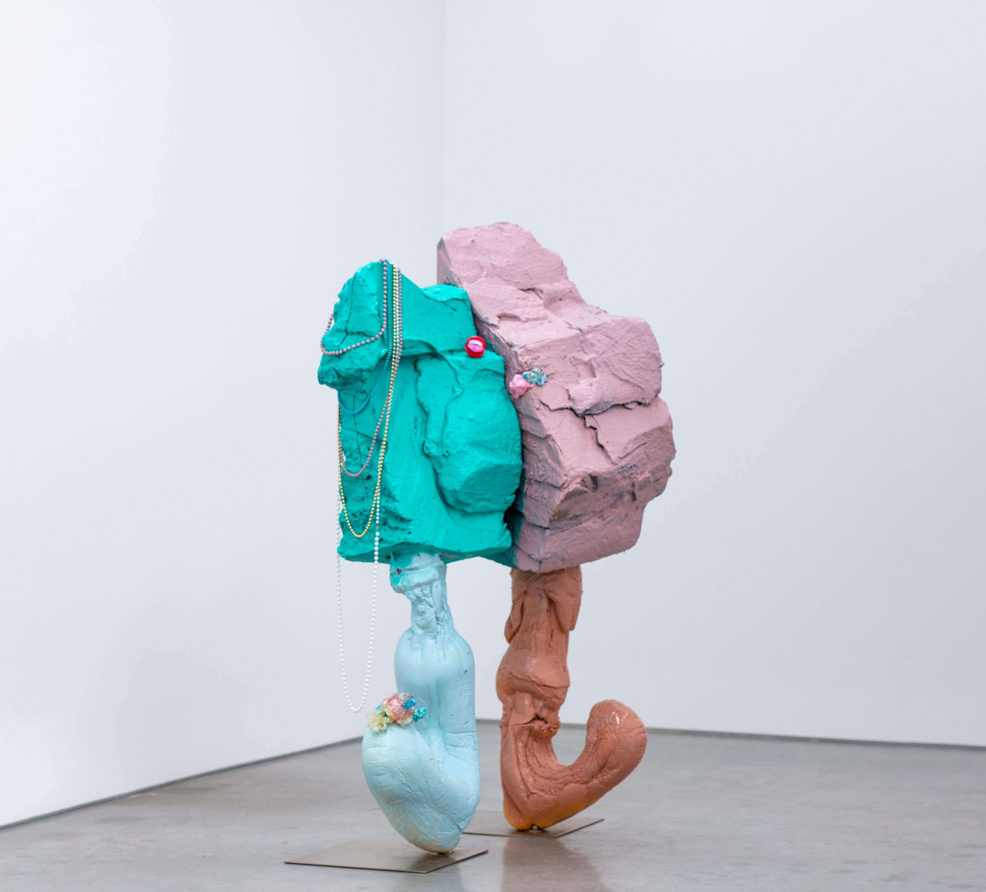 A sculpture made from clay, stell and foam, and painted in bright colours, like two rocks stuck together, with legs.