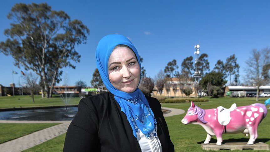 Zahra wearing a blue hijab pictured with a lake and pink cow statue behind her.