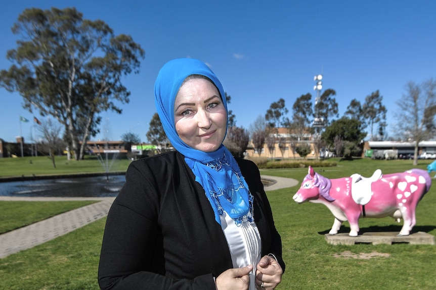 Zahra wearing a blue hijab pictured with a lake and pink cow statue behind her.