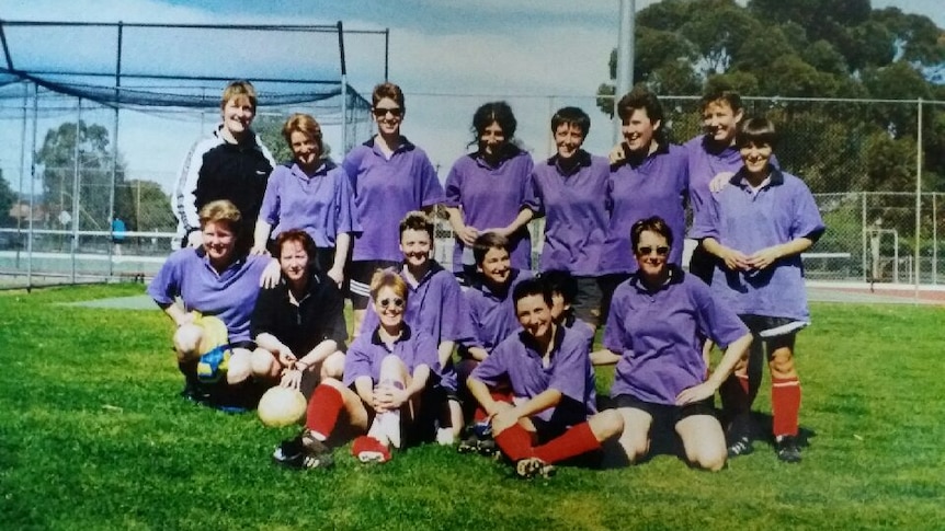 A group of female soccer players wearing purple shirts and red socks pose for a photo