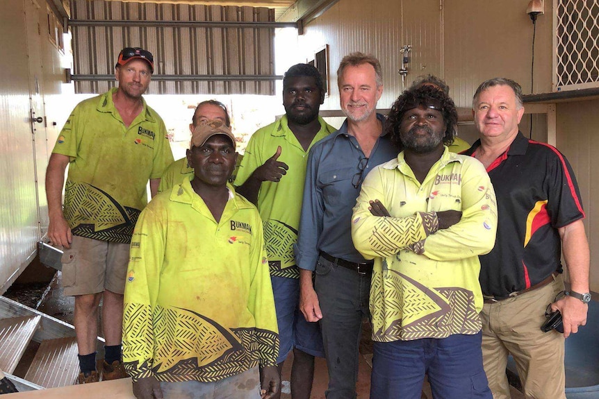 A group of Aboriginal men in work clothes stand with Nigel Scullion