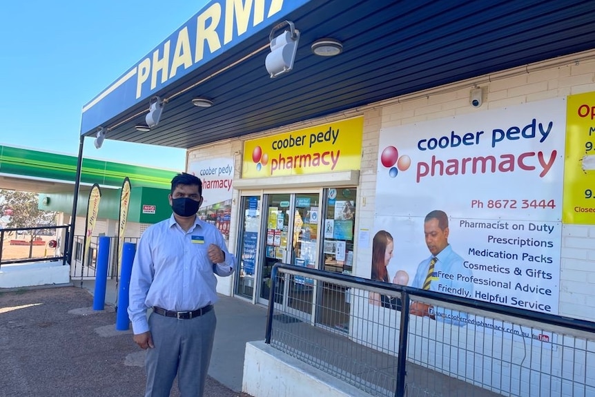 A man wearing a mask standing behind a pharmacy.