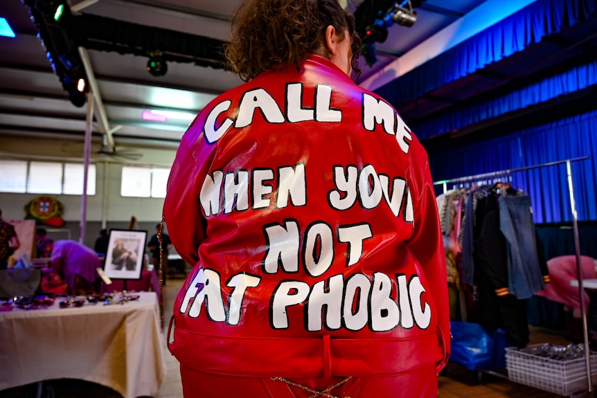 A persons showing the back of their read leather jacket which read ‘call me when you’re not fatphobic’.