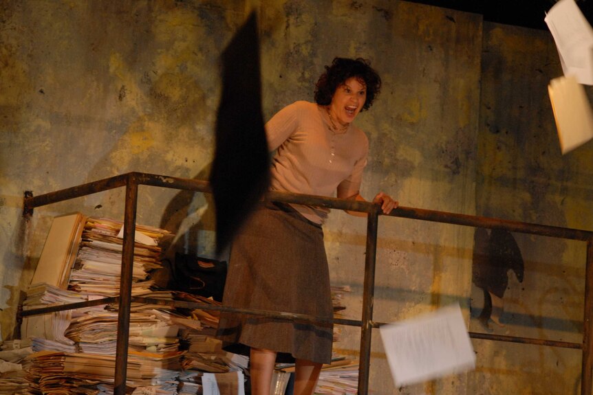 The actor Leah Purcell on stage dressed in tan inmate clothes and throwing papers