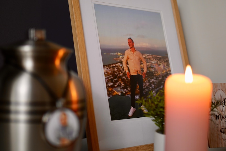 A framed photo of a young man sits behind a burning candle.