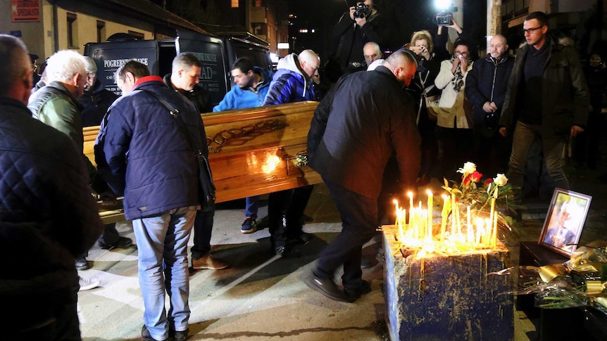 People carry the coffin of Oliver Ivanovic in front of his office, where there are also candles lit and a framed photo of him.