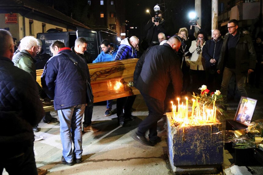 People carry the coffin of Oliver Ivanovic in front of his office, where there are also candles lit and a framed photo of him.